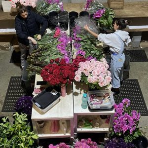 Two florists preparing bunches at a busy workbench with fresh flowers