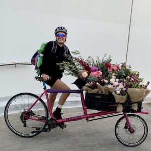 Bike courier on pink bicycle with overflowing bunches of flowers