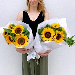 Florist holding two bright bunches of sunflowers.