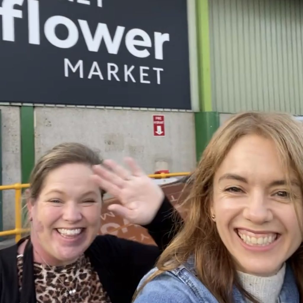 Two team members smiling in front of Sydney Flower Market sign