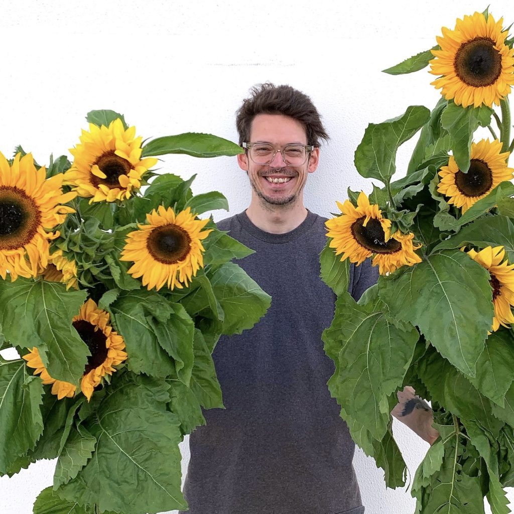 Man smiling while holding two large bunches of bright yellow sunflowers