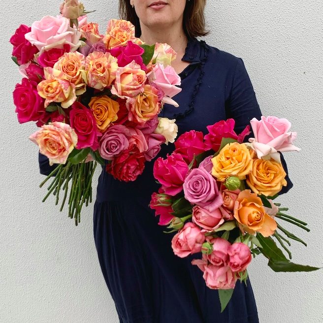 Woman holding two large bunches of vibrant garden roses against a white wall