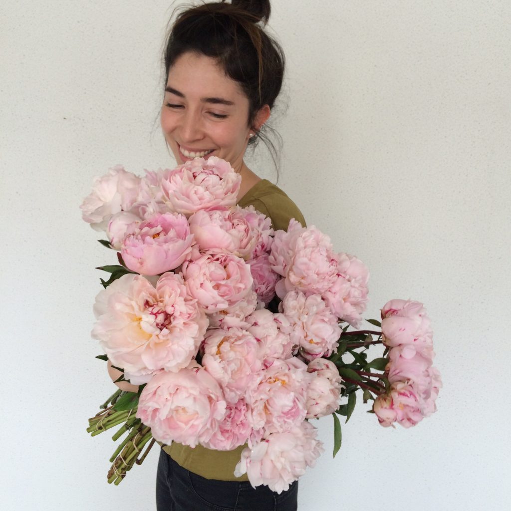 Woman smiling while holding a large armful of pink peonies