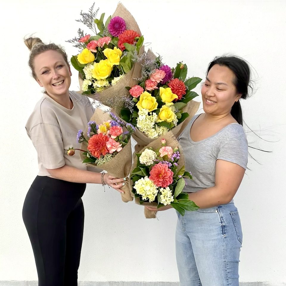 Two smiling florists holding bright mixed bunches with roses and dahlias