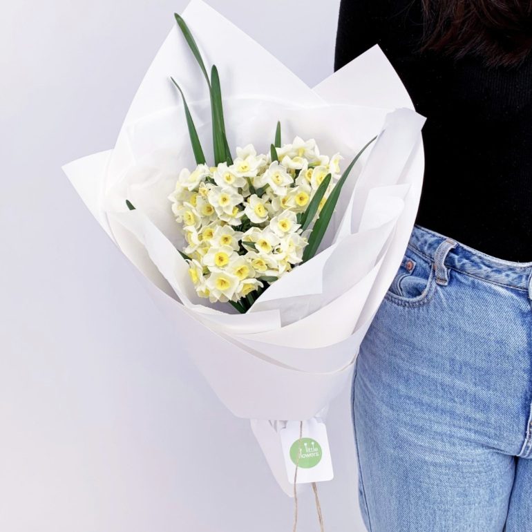 Wrapped bouquet of white and yellow jonquils held by a woman in jeans
