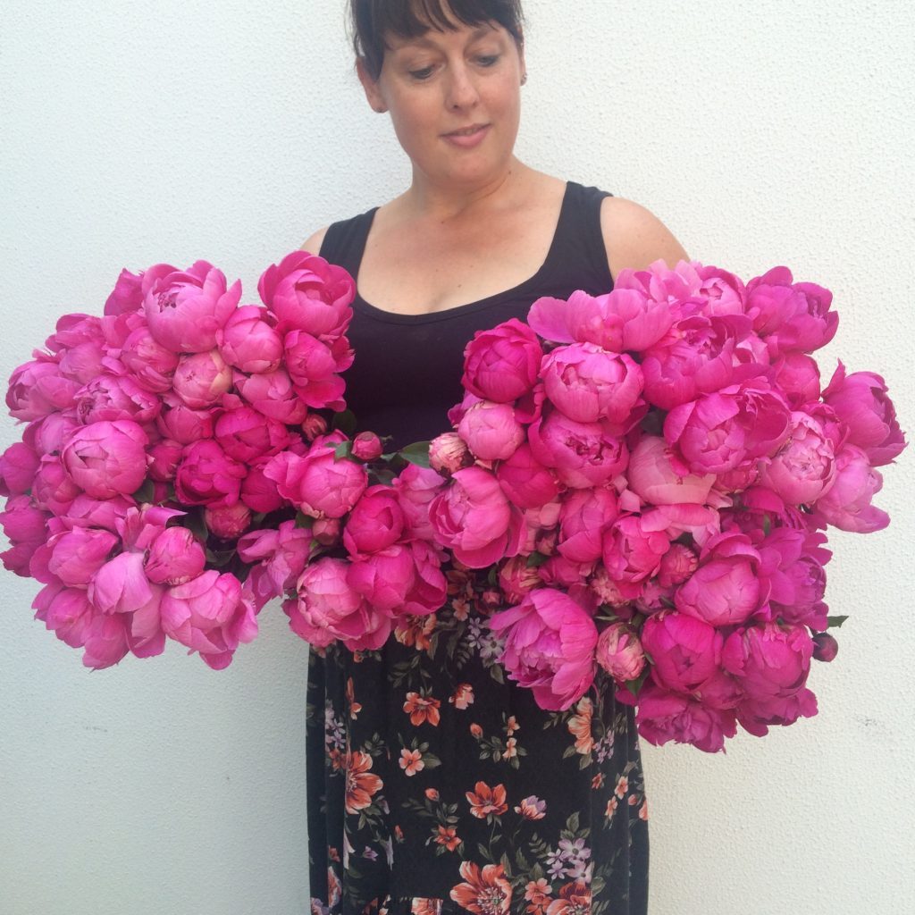 Woman holding large bunches of bright pink peonies