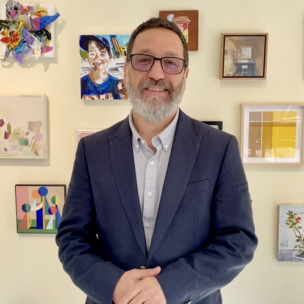 Dr Tim Sharp smiling in front of framed artworks