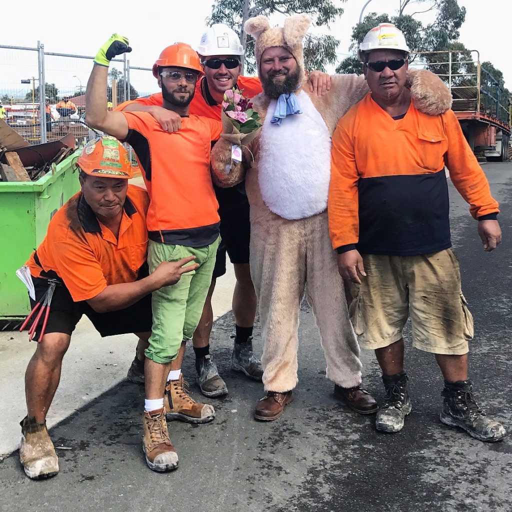 A man in an Easter bunny costume delivering flowers to construction workers, all smiling and posing together
