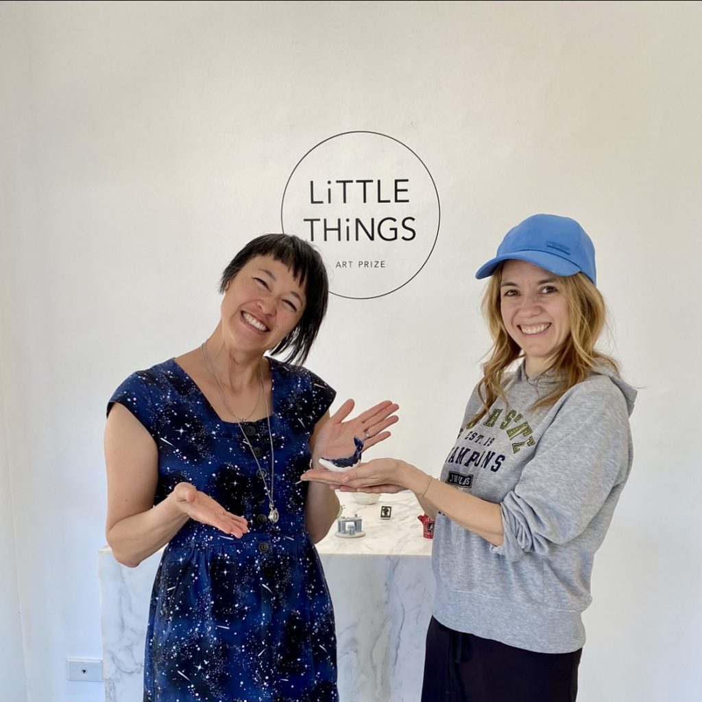 Two women smiling in front of the Little Things logo