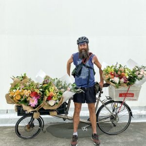 Joe standing proudly beside a cargo bike loaded with flowers